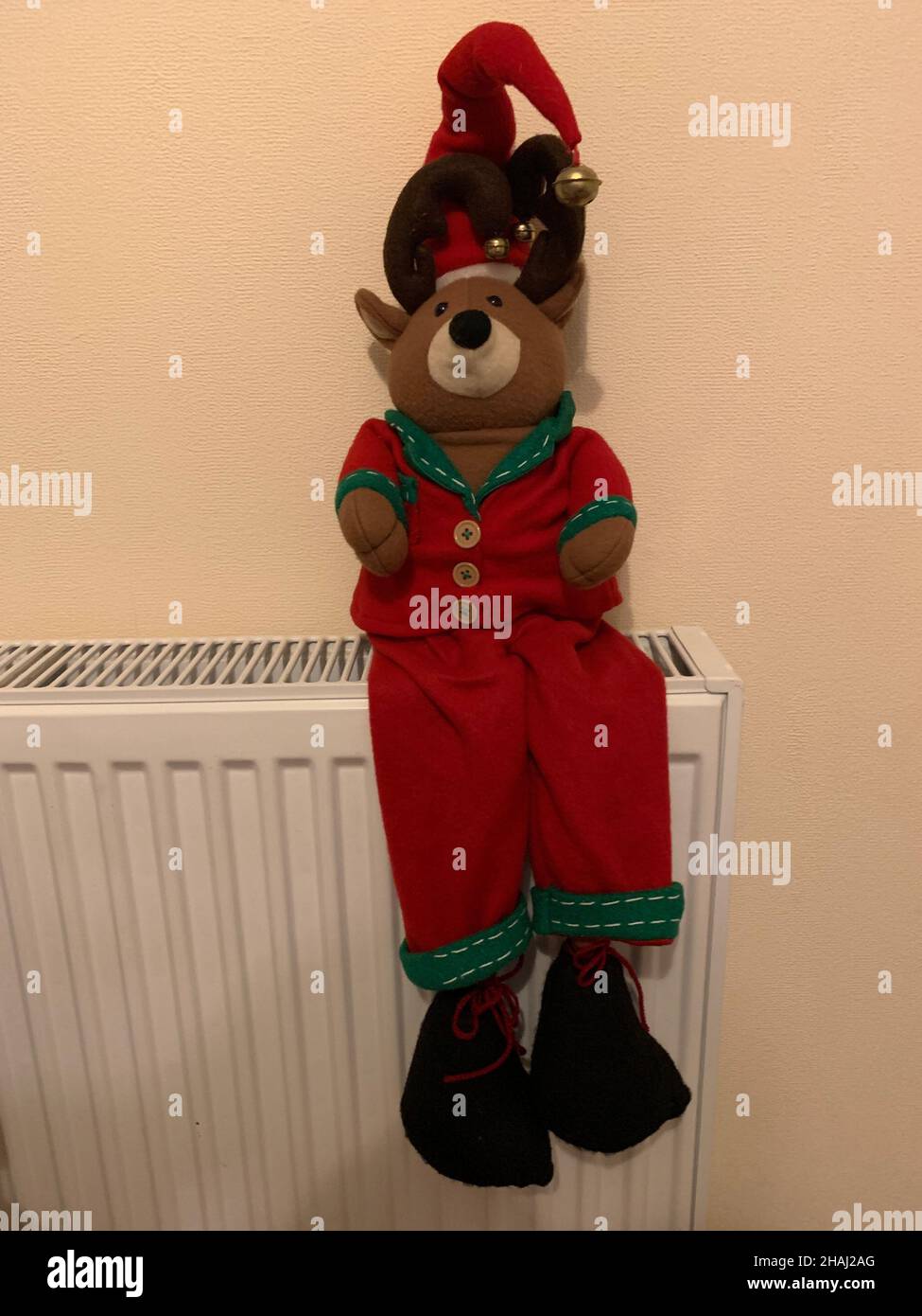 Ornamenti di Natale seduti su un radiatore con cappello rosso su e giacca rossa con campane su cappello scarpe nere sopportare seduto caldo accogliente luminoso colori rosso Foto Stock