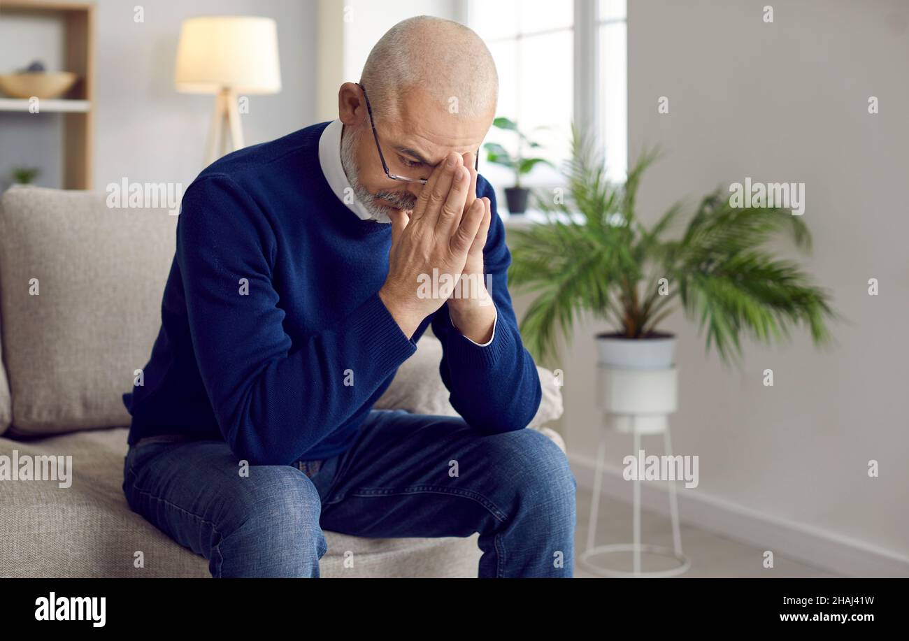 L'anziano, stressato e preoccupato, seduto sul divano, pregando Dio e chiedendo aiuto Foto Stock