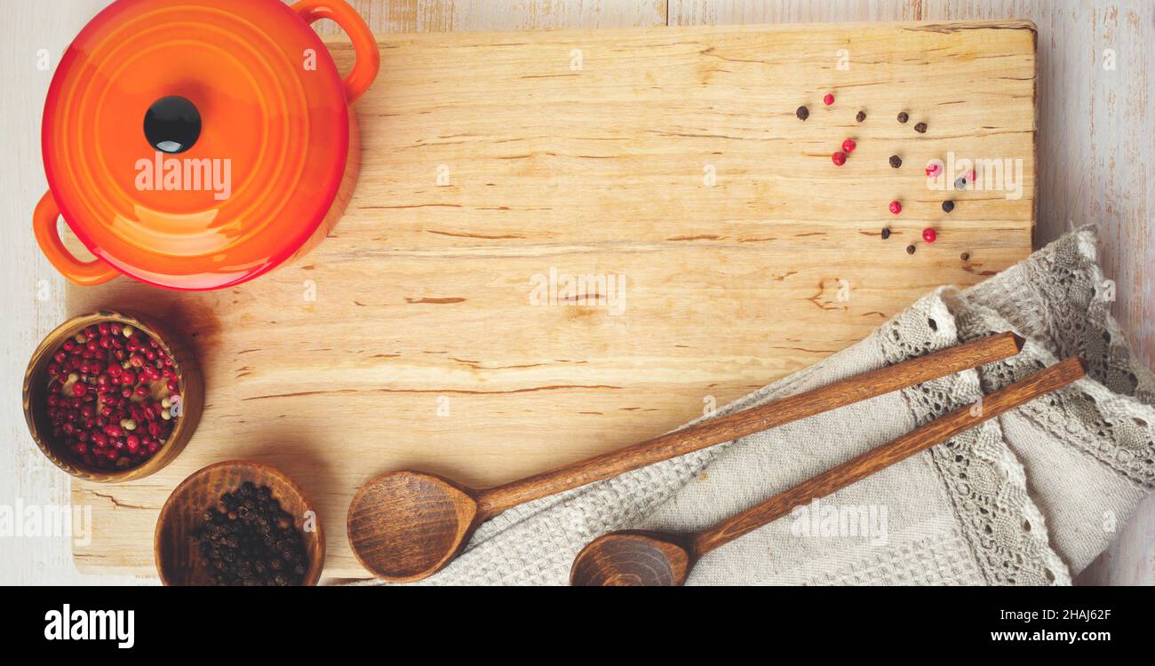 Pepe nero e rosso, foglie di basilico, teglia in ceramica, stativo in legno, cucchiai semplici e tovagliolo in lino su sfondo chiaro. Concetto di accessori per la cucina. Se Foto Stock