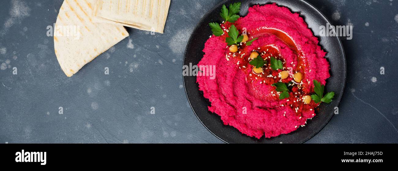 Hummus di barbabietole fatto in casa in ceramica nera su vecchio fondo di cemento scuro. Messa a fuoco selettiva. Vista dall'alto. Foto Stock