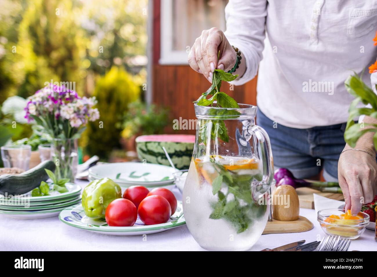 Donna che mette l'erba della menta in limonata fredda in caraffa. Preparazione di bevande analcoliche per feste in giardino Foto Stock