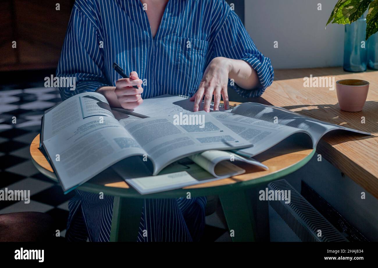 Le mani femminili che tengono la penna e leggono il lotto dei libri. Concetto di ricerca e ricerca di risposte nei libri di testo. Foto Stock