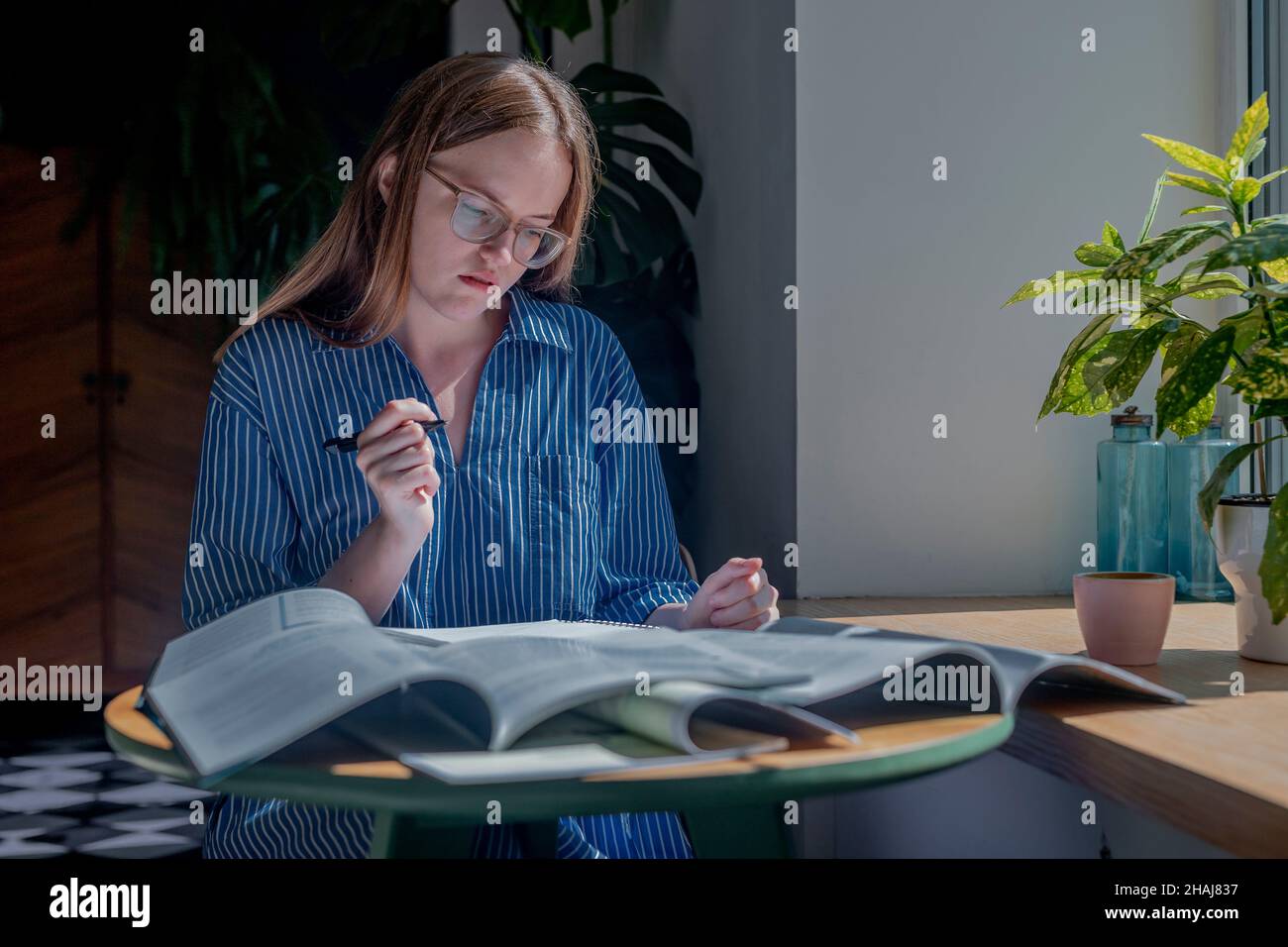Donna che tiene la penna e leggere libri heap sul banco in caffetteria. Concetto di ricerca e ricerca di risposte in letteratura. Foto Stock