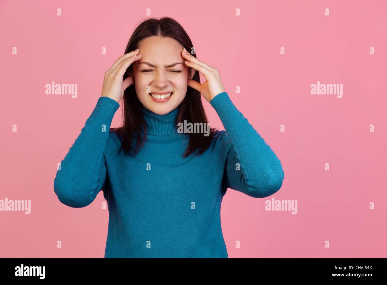 Una ragazza emozionale in caldo maglione blu inverno isolato su sfondo rosa studio. Concetto di emozioni Foto Stock