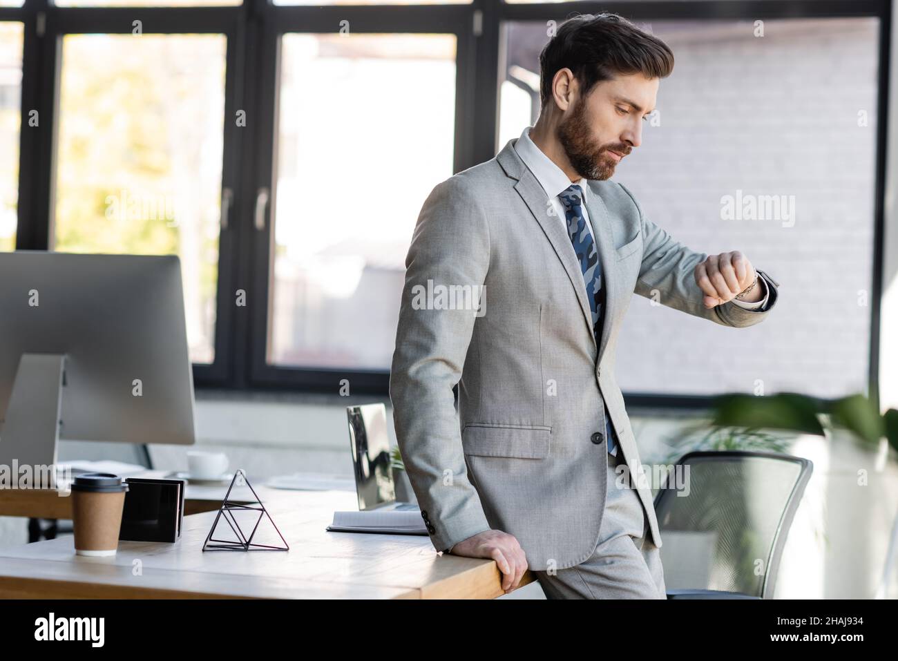 Uomo d'affari che guarda il orologio da polso vicino ai computer in ufficio Foto Stock
