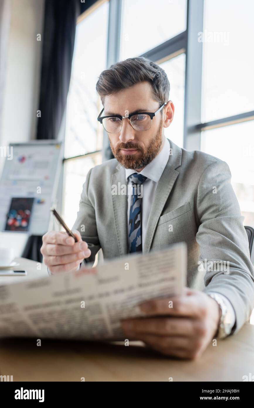 Uomo d'affari in occhiali lettura blurred giornale in ufficio Foto Stock
