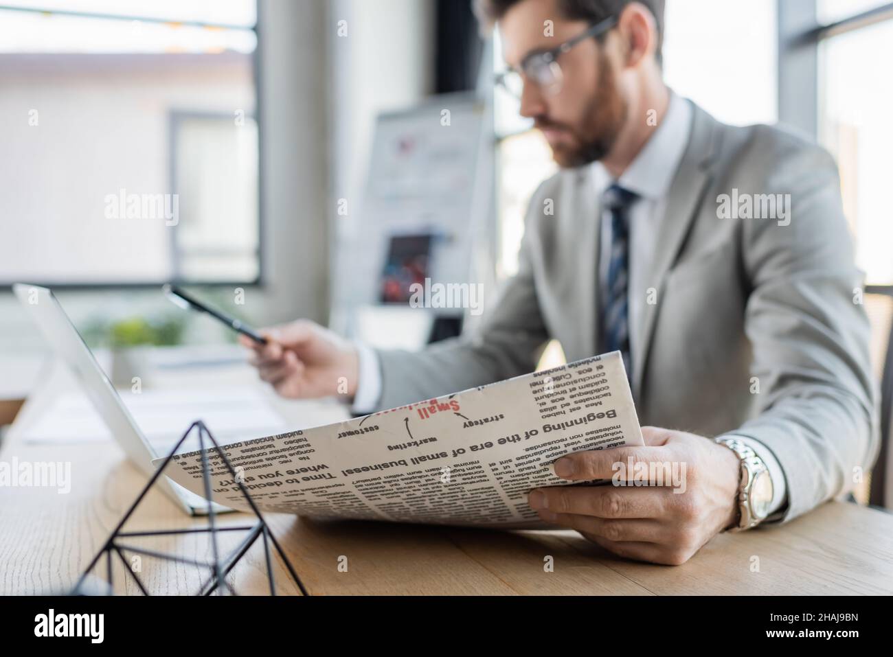 Giornale in mano di uomo d'affari blurred che lavora in ufficio Foto Stock