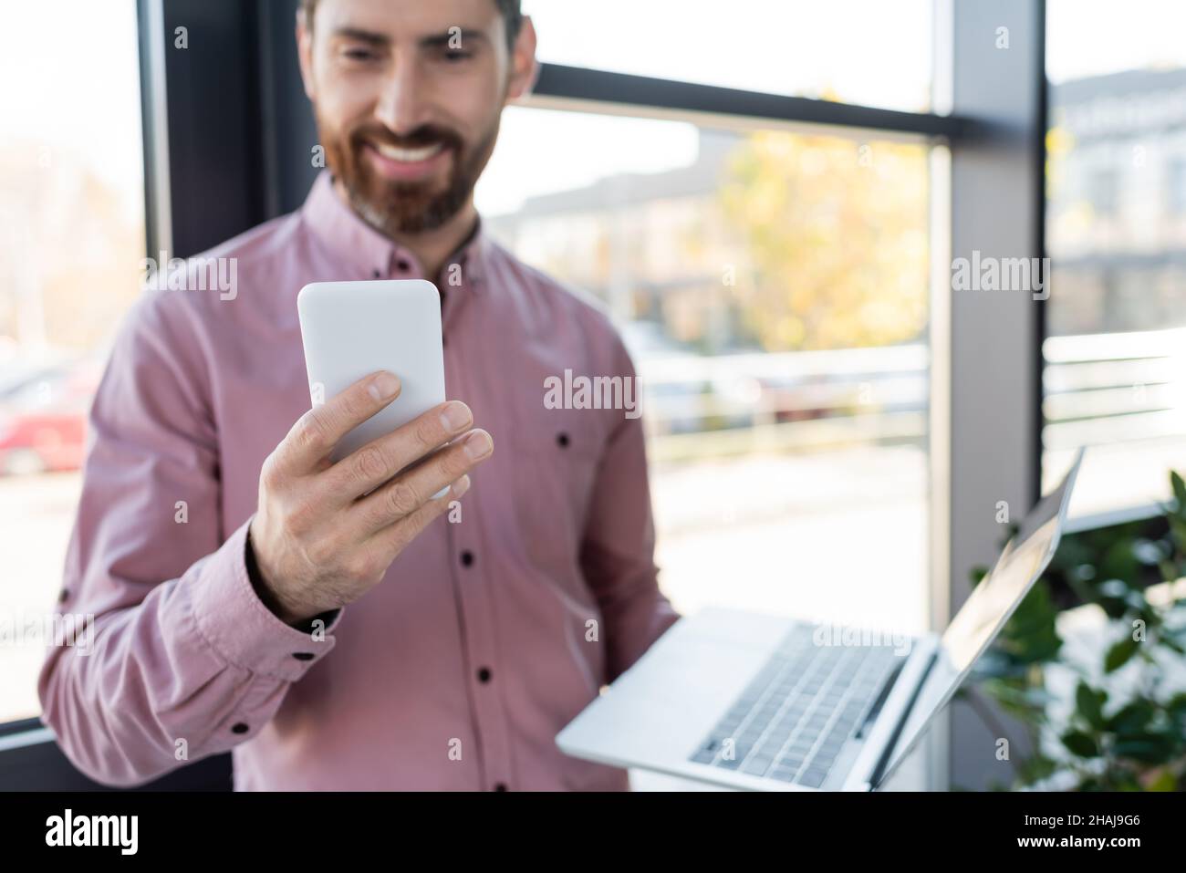 Smartphone in mano a un uomo d'affari offuscato con un notebook in ufficio Foto Stock