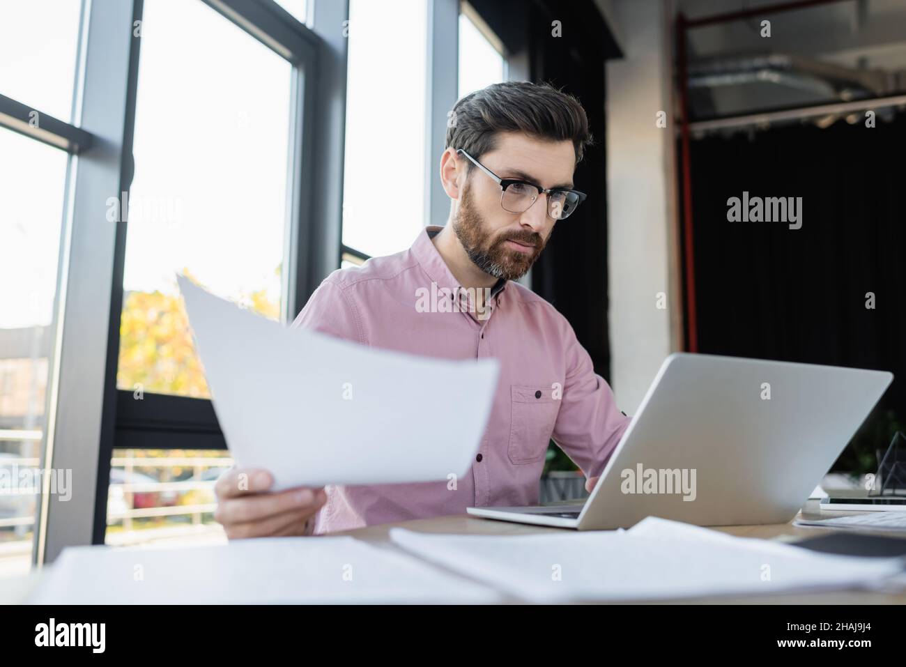 Uomo d'affari in occhiali che lavora con carte e laptop in ufficio Foto Stock