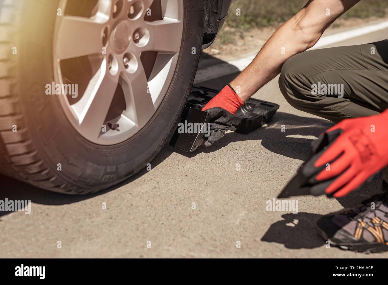 Calzatoie per ruote sotto lo pneumatico dell'auto su strada, mani del conducente. Foto Stock