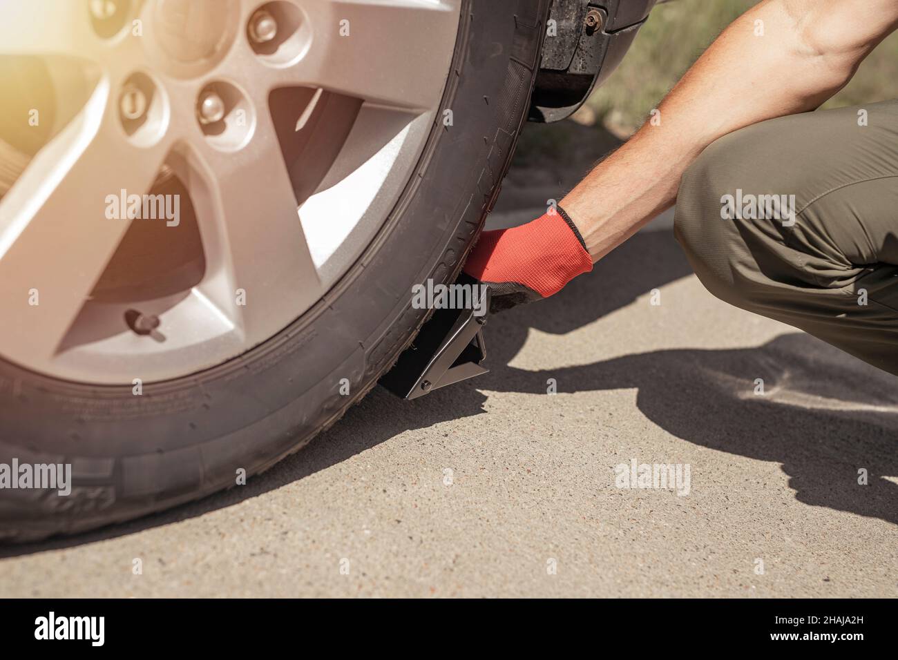 Uomo che mette i cunei della ruota sotto la ruota dell'automobile su strada, primo piano. Foto Stock