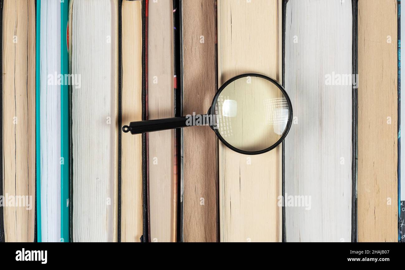 Lente di ingrandimento sopra la pila di libri con molte pagine. Concetto di ricerca e indagine in biblioteca. Foto Stock
