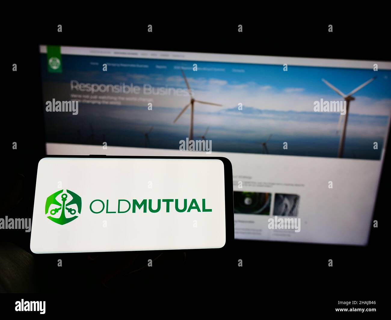 Persona che tiene il cellulare con il logo della società finanziaria africana Old Mutual Limited (OML) sullo schermo di fronte al sito web. Mettere a fuoco sul display del telefono. Foto Stock