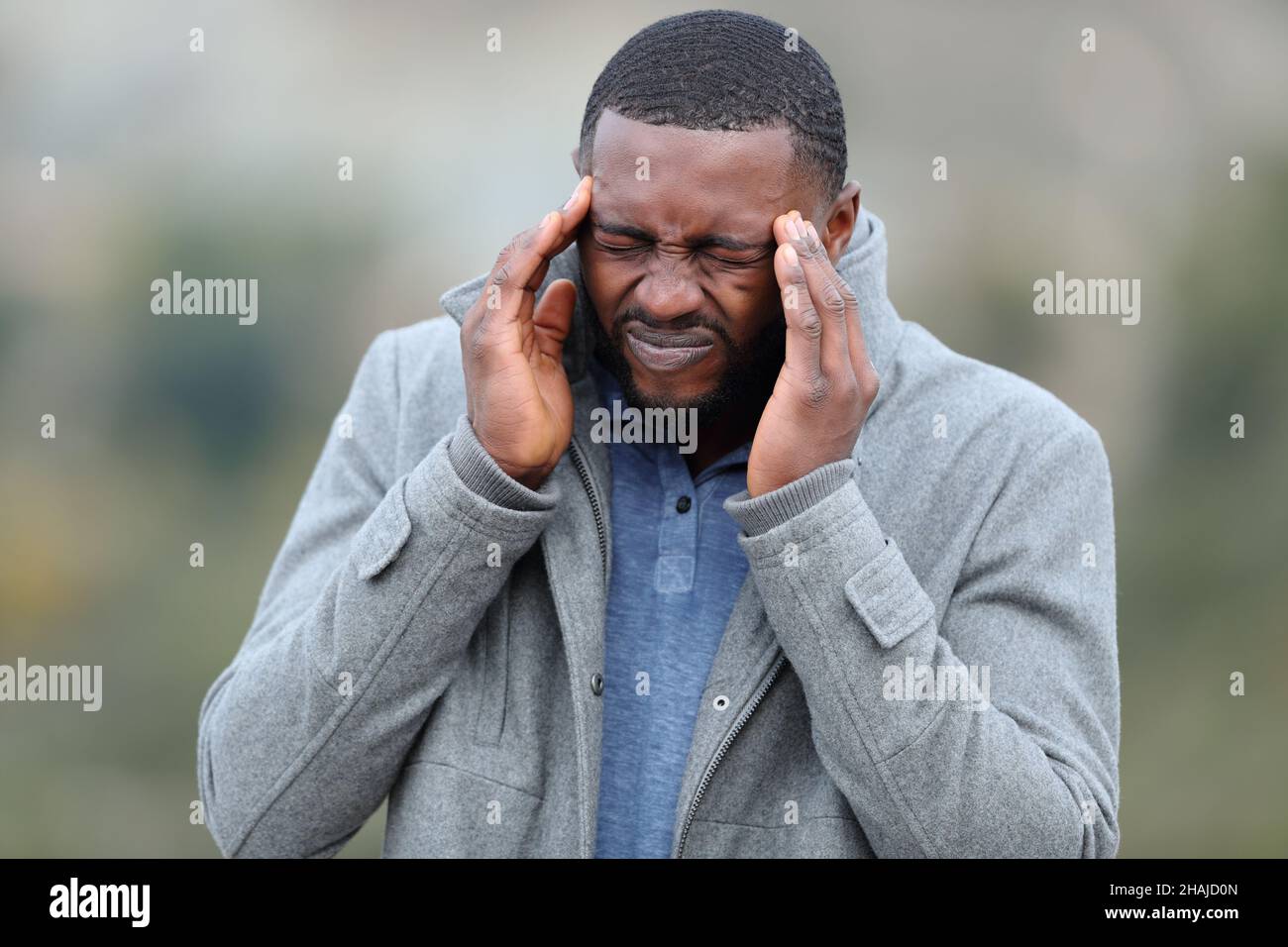 Uomo stressato con pelle nera che soffre emicrania all'aperto in inverno Foto Stock