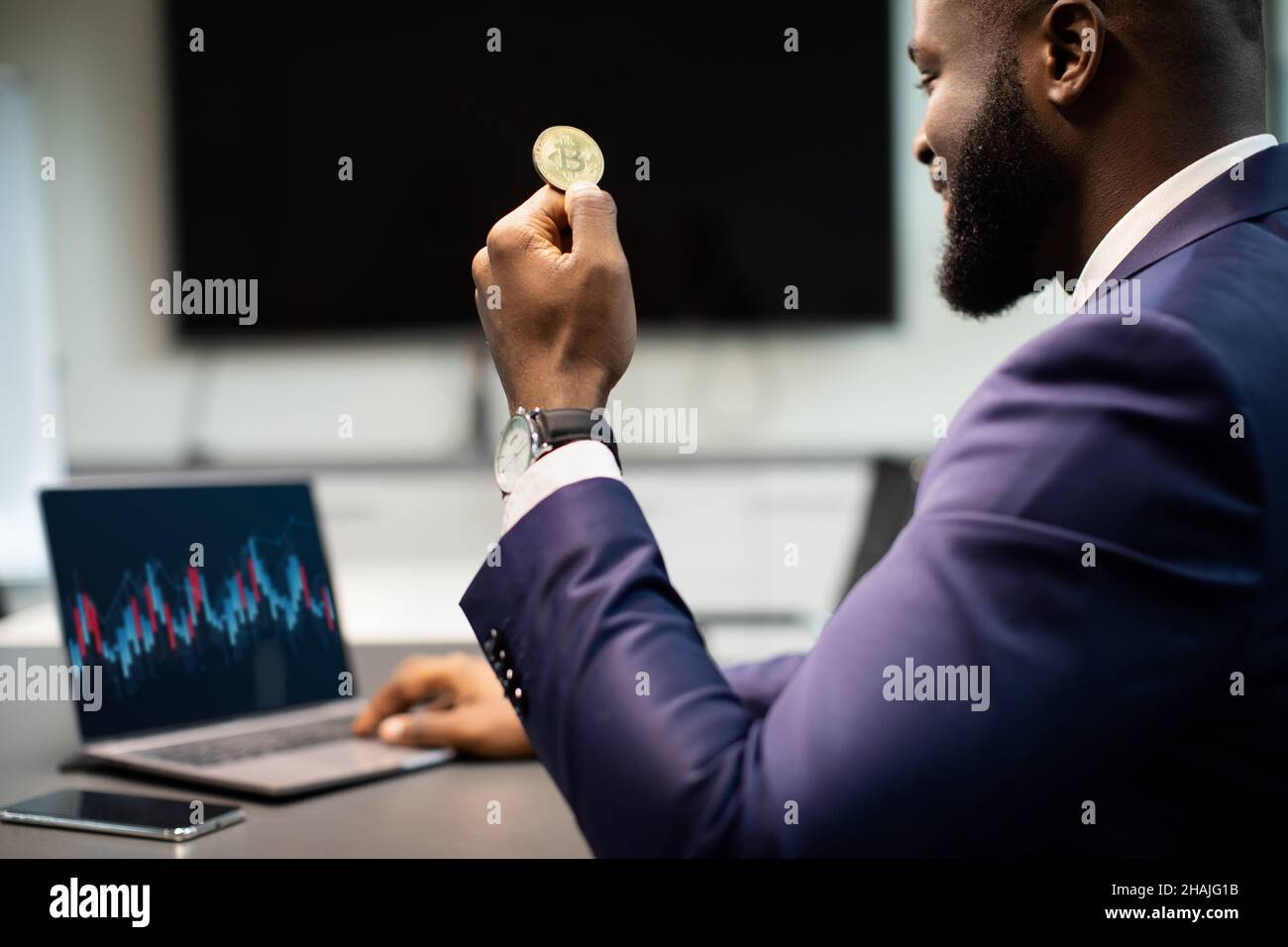 Primo piano di un imprenditore afroamericano che tiene bitcoin, utilizzando un computer portatile Foto Stock