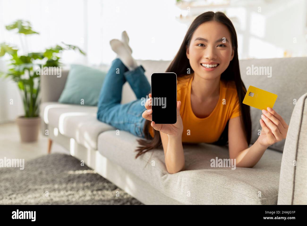 Eccitata signora asiatica mostrando il cellulare con schermo vuoto e carta di credito, mostrando mockup per il disegno di Web site o l'annuncio Foto Stock