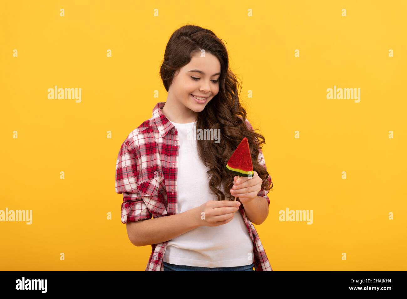 sorridente capretto con capelli ricci lunghi tenere lecca lecca caramello caramella su sfondo giallo, dente dolce. Foto Stock