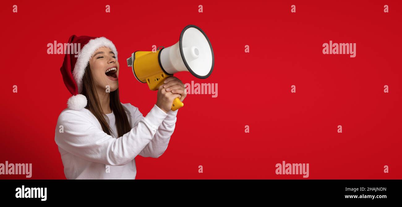 Donna in Santa Hat fare annuncio di Natale con altoparlante su sfondo rosso Foto Stock