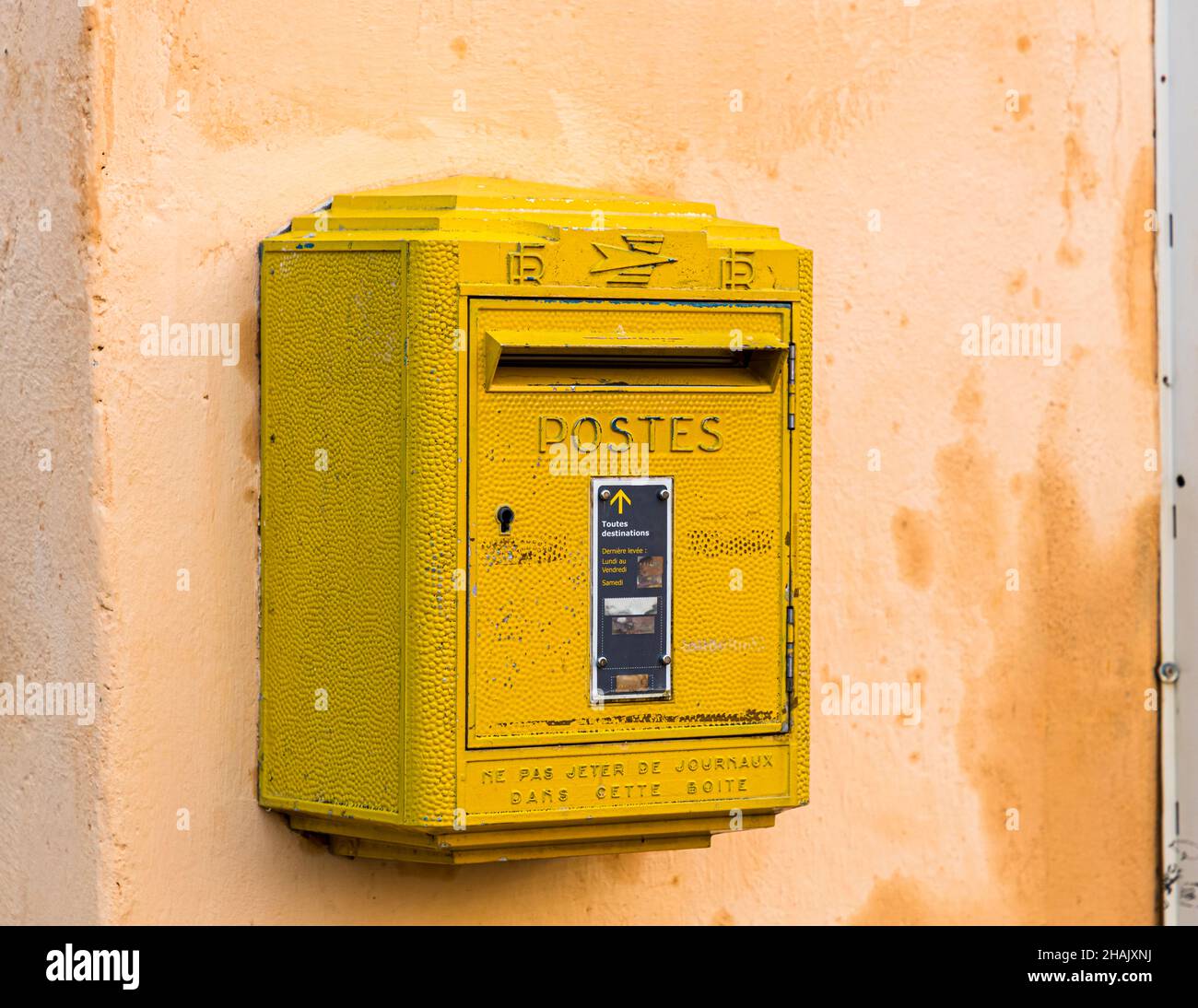 Una cassetta postale francese gialla è appesa a un muro di casa color ocra a Tourtour, dipartimento di Var, Francia. Foto Stock