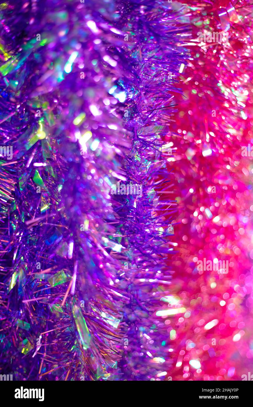 Tinsel natalizio di lilla e rosa, sfondo iridescente sfocato verticale con bokeh. Arredamento festivo. Foto Stock