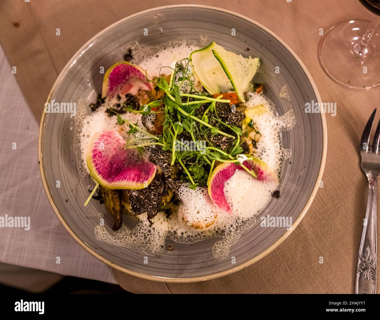 Trifola nera affumicata copre un piatto brasato con una salsa schiumosa in un bistrot ad Aups, dipartimento di Var, Francia; ravanelli di anguria e germogli di pisello guarniscono il piatto. Foto Stock