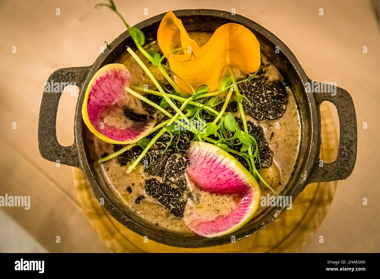 Il tartufo nero è disposto a fette sottili su una base cremosa in una pentola di ghisa in un bistrot ad Aups, dipartimento di Var, Francia; ravanello melone, germogli di piselli e una ricciolina di carota guarniscono il piatto. Foto Stock