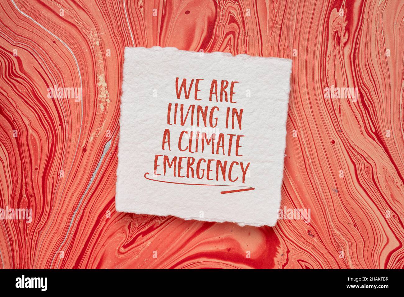 viviamo in clima emergenza parola astratto, scrittura a mano su una carta fatta a mano contro la carta marmorizzata rossa, concetto di riscaldamento globale Foto Stock