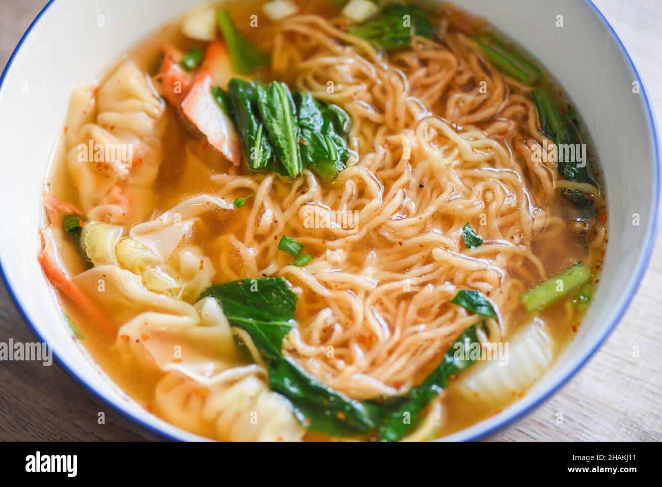 spaghetti per zuppa, spaghetti gialli di maiale wonton con gnocchi di maiale arrostiti rossi e verdure cinesi al brace in ciotola per zuppa su tavolo di legno, vista dall'alto Foto Stock