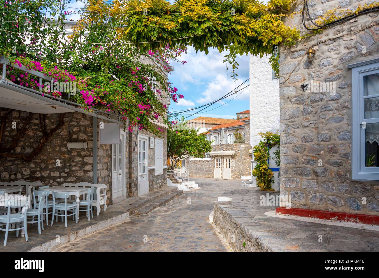 Una strada pittoresca di pietra e case dipinte di bianco e un piccolo caffè all'aperto nel villaggio della piccola isola greca di Hydra, Grecia. Foto Stock