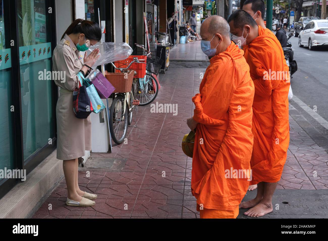 Un dipendente dell'autorità Metropolitana di Bangkok in uniforme 'wai-ing' (saluto rispettosamente) monaci buddisti nel loro turno di elemosina; Bangkok, Thailandia Foto Stock