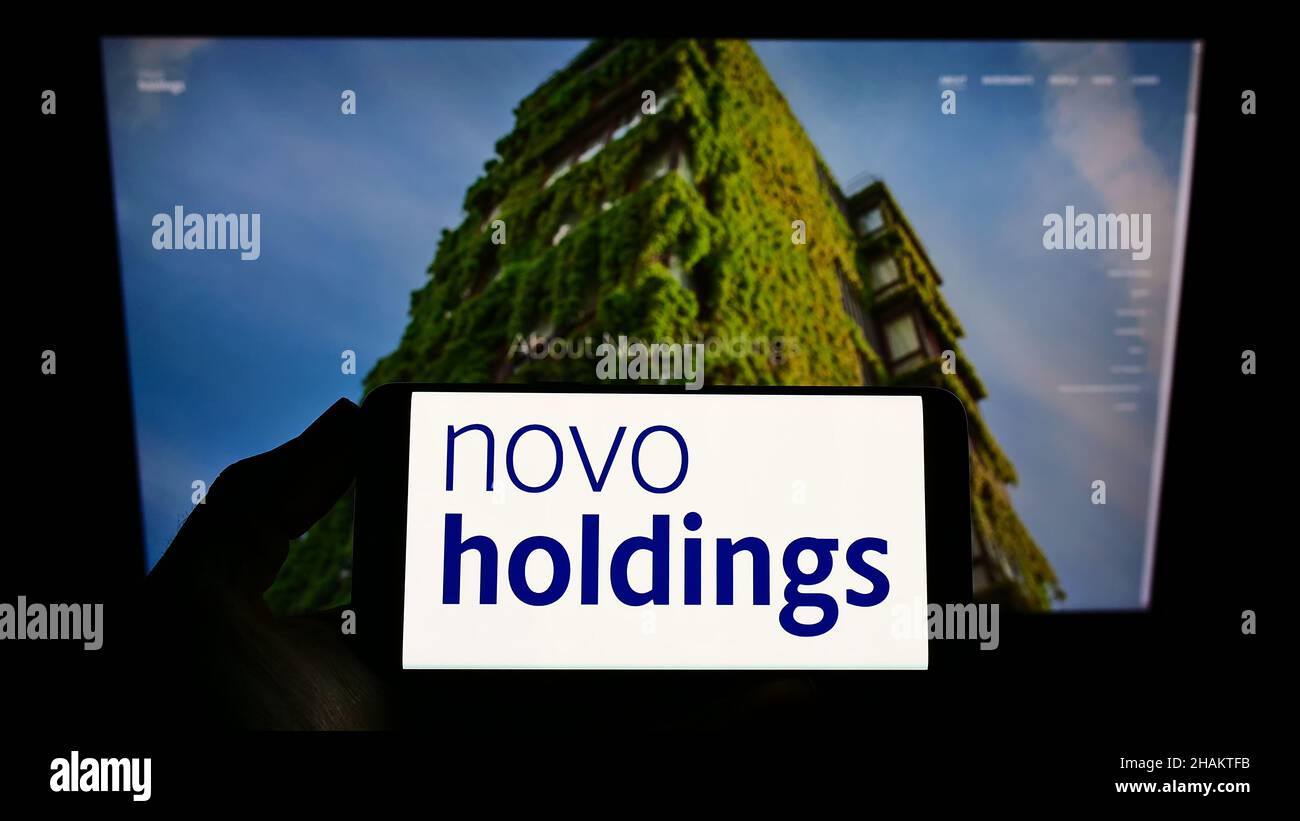 Persona che detiene smartphone con il logo della società di investimento danese Novo Holdings SULLO schermo di fronte al sito web. Mettere a fuoco sul display del telefono. Foto Stock