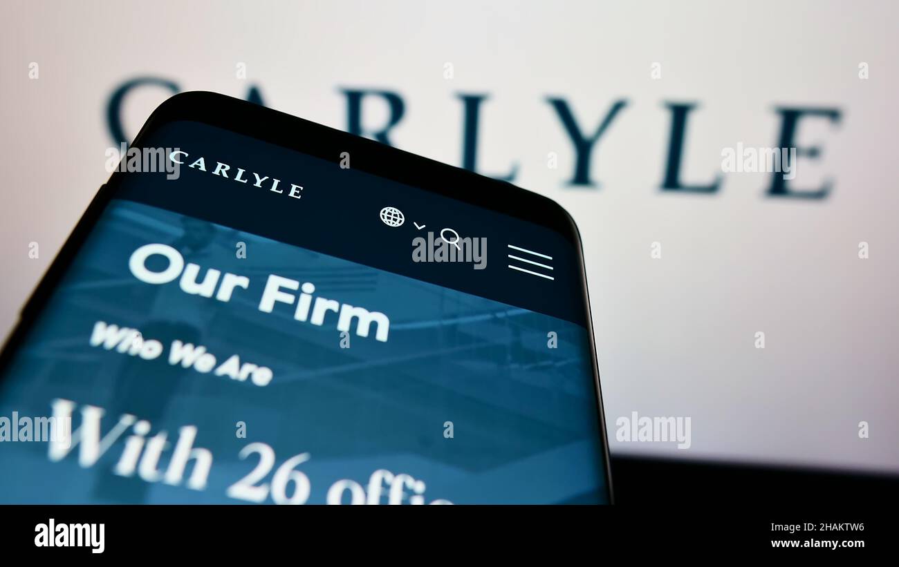 Persona che detiene smartphone con sito web della società di investimento il Gruppo Carlyle L.P. sullo schermo di fronte al logo. Concentrarsi sul centro del display del telefono. Foto Stock