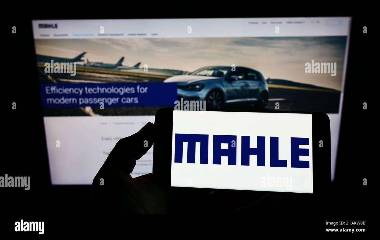 Persona che tiene uno smartphone con il logo del fornitore automobilistico tedesco MAHLE GmbH sullo schermo di fronte al sito web. Mettere a fuoco sul display del telefono. Foto Stock