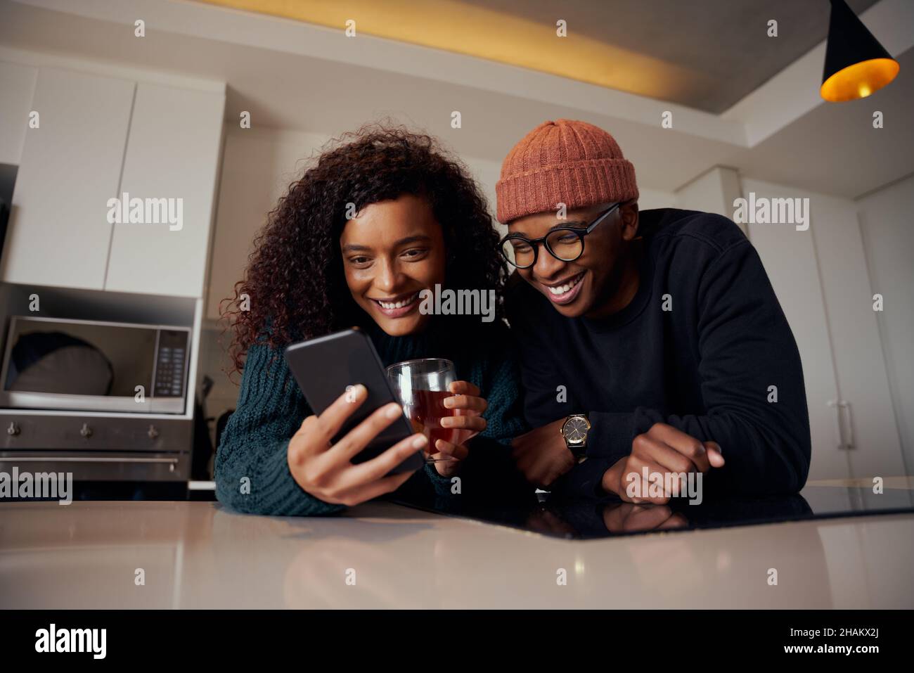 Coppia multietnica ridendo e sorridendo al telefono mentre in cucina in appartamento moderno Foto Stock