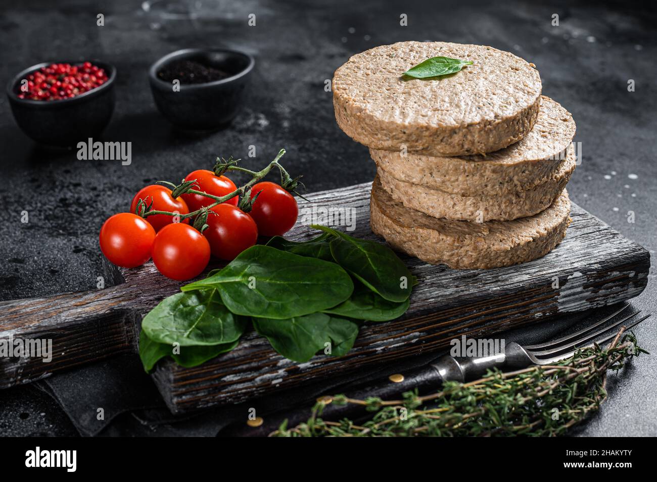 Polpettine vegetariano a base di carne di hamburger, cotolette vegane crude su tavola di legno con erbe. Sfondo nero. Vista dall'alto Foto Stock