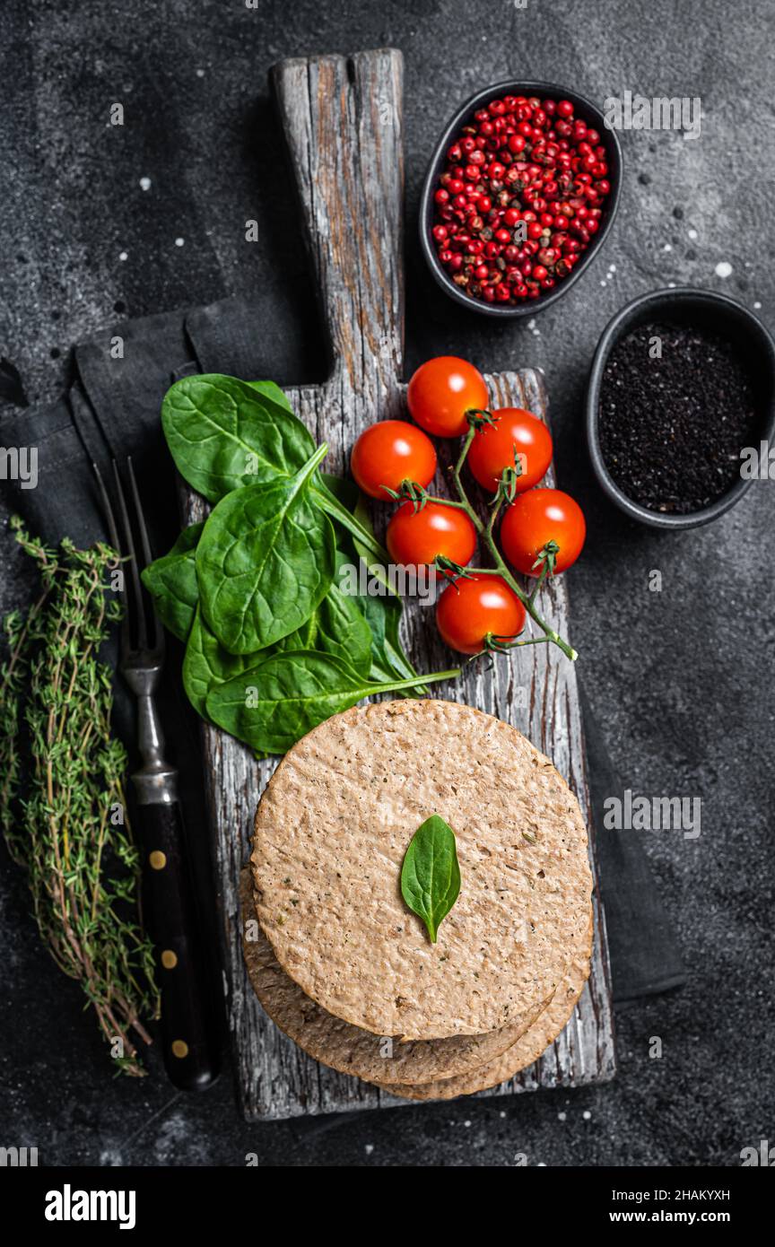 Polpettine vegetariano a base di carne di hamburger, cotolette vegane crude su tavola di legno con erbe. Sfondo nero. Vista dall'alto Foto Stock