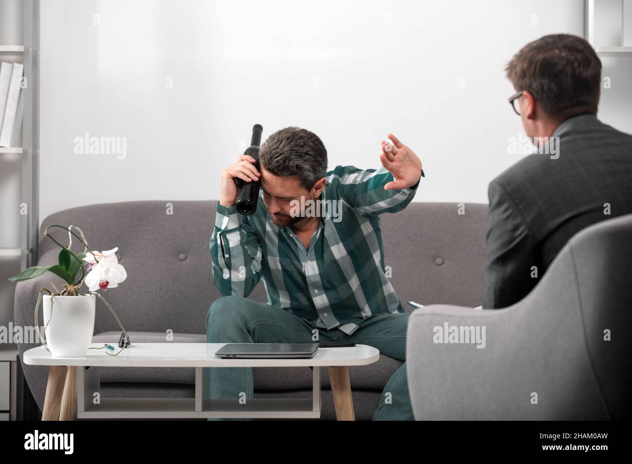 Uomo depresso con bottiglia di vino in sessione di psicoterapia. Abuso delle persone e problemi di alcolismo. Psicologia, concetto di terapia mentale. Foto Stock