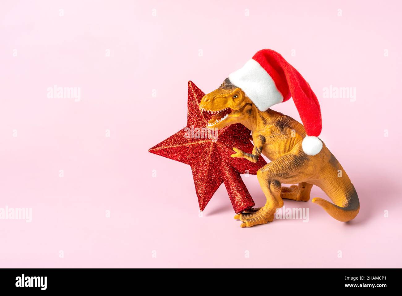Il Rex del dinosauro in cappello rosso di Babbo Natale tiene la stella nelle relative zampe su sfondo rosa la vigilia di Capodanno o la vigilia di Natale scheda di festa d'arte creativa idea per Merry Foto Stock