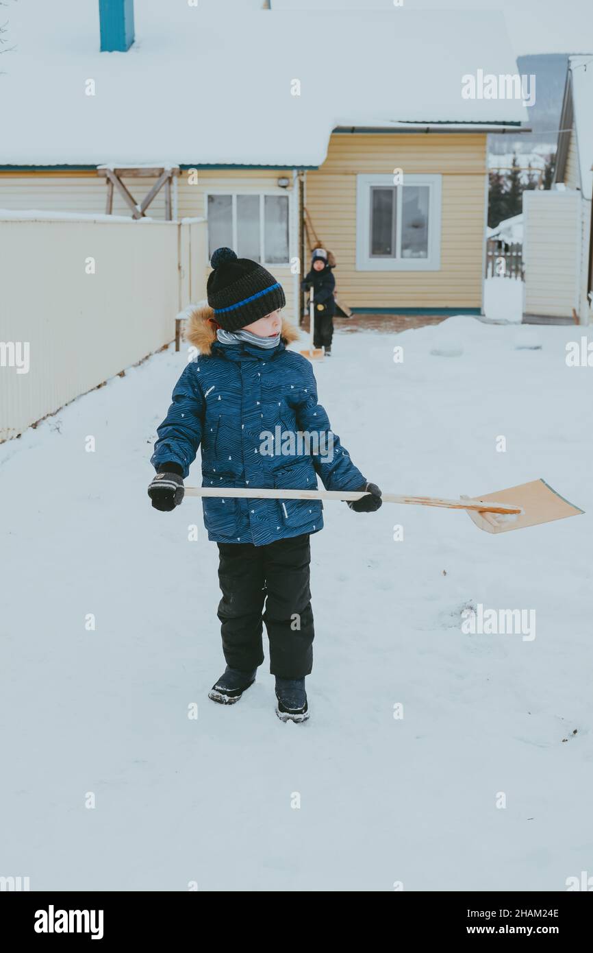 ragazzo pulisce la neve con una pala per strada. Un ragazzo libera la strada dalla neve in inverno. Bambino che lavora duramente. Un ragazzo che vive nel villaggio pulisce la neve Foto Stock