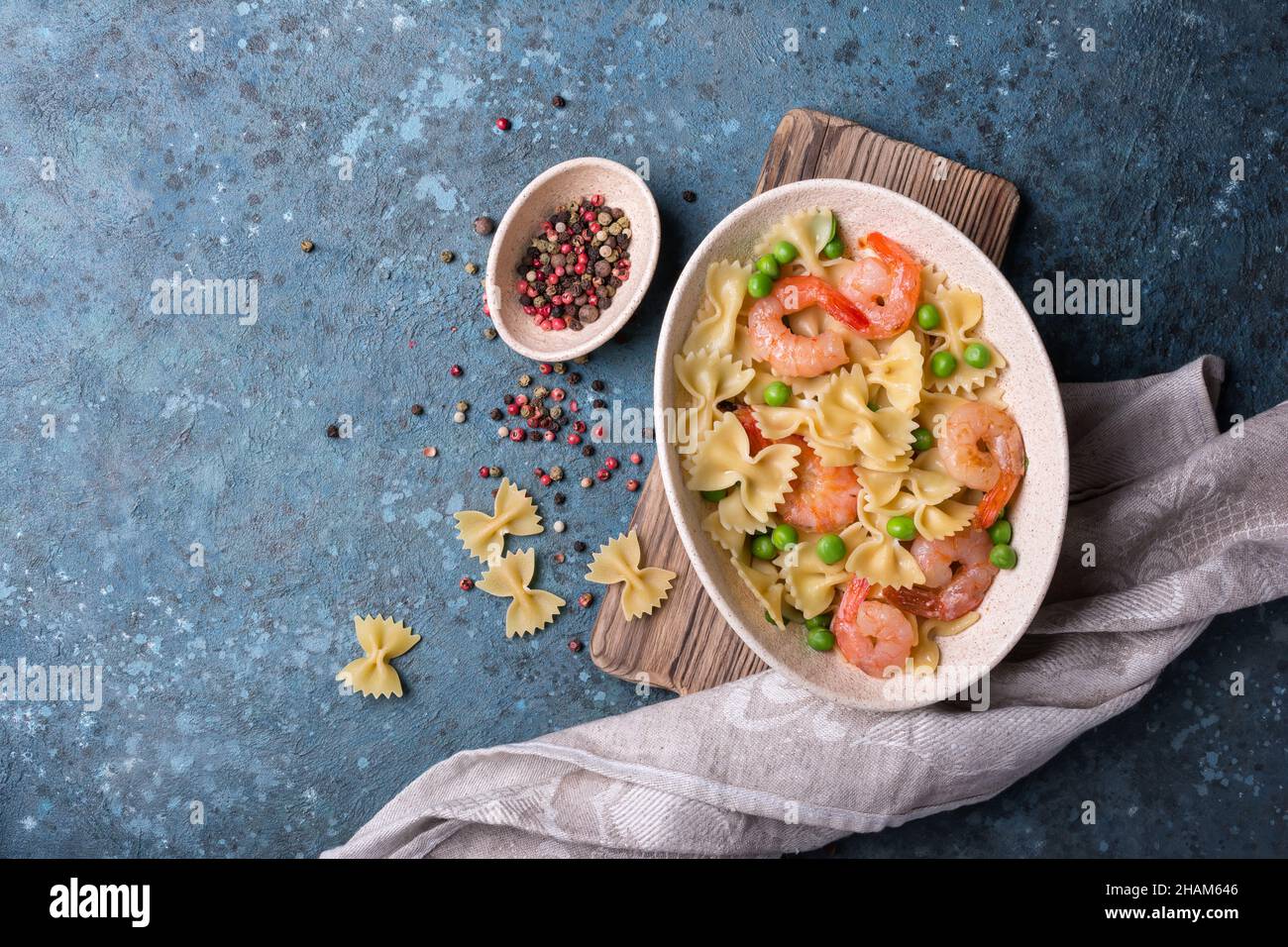 Vista dall'alto della gustosa pasta di farfalle italiana con gamberi o gamberi e piselli verdi su sfondo blu di cemento Foto Stock