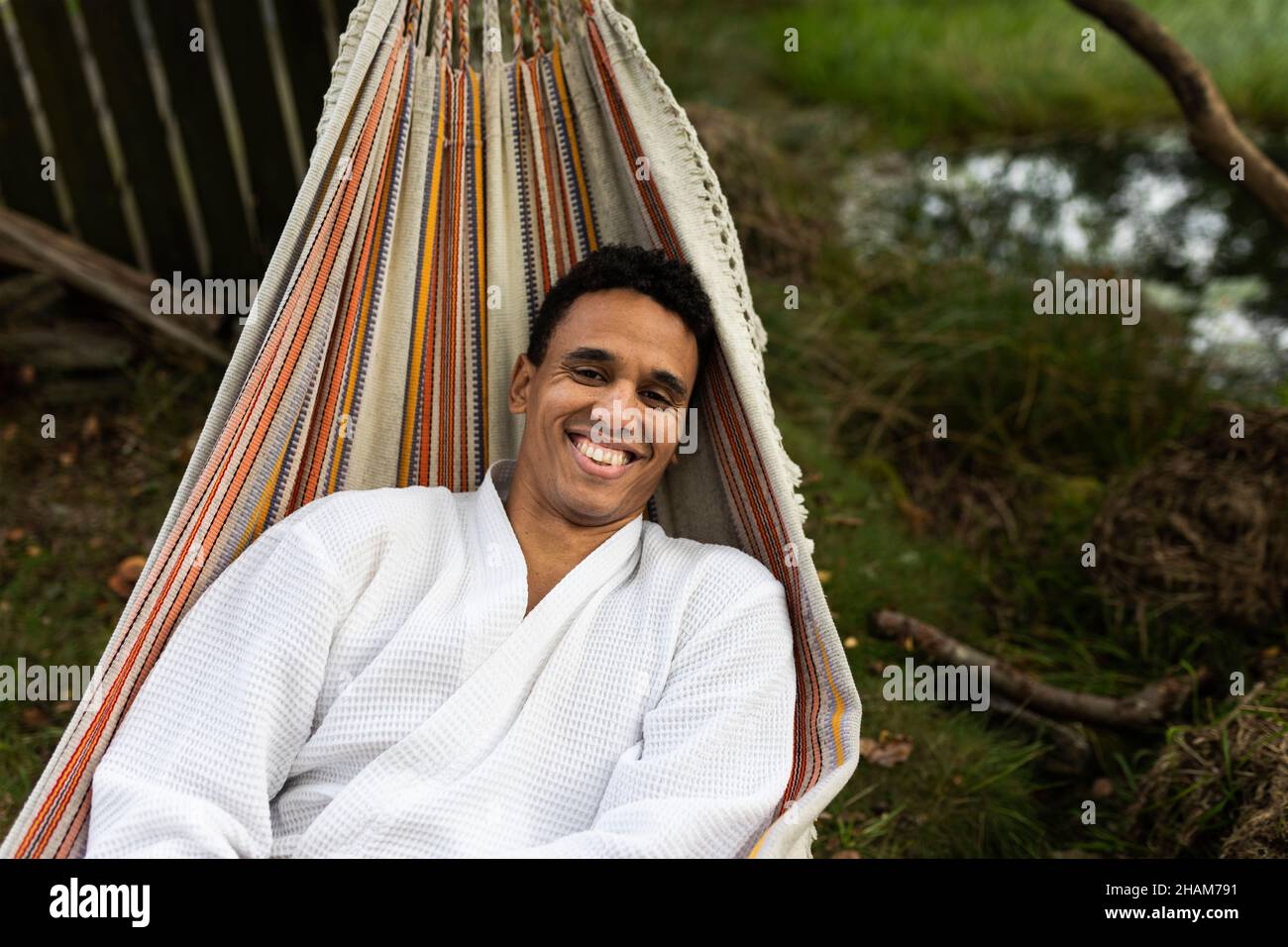 Giovane uomo sorridente in accappatoio rilassante in amaca Foto Stock