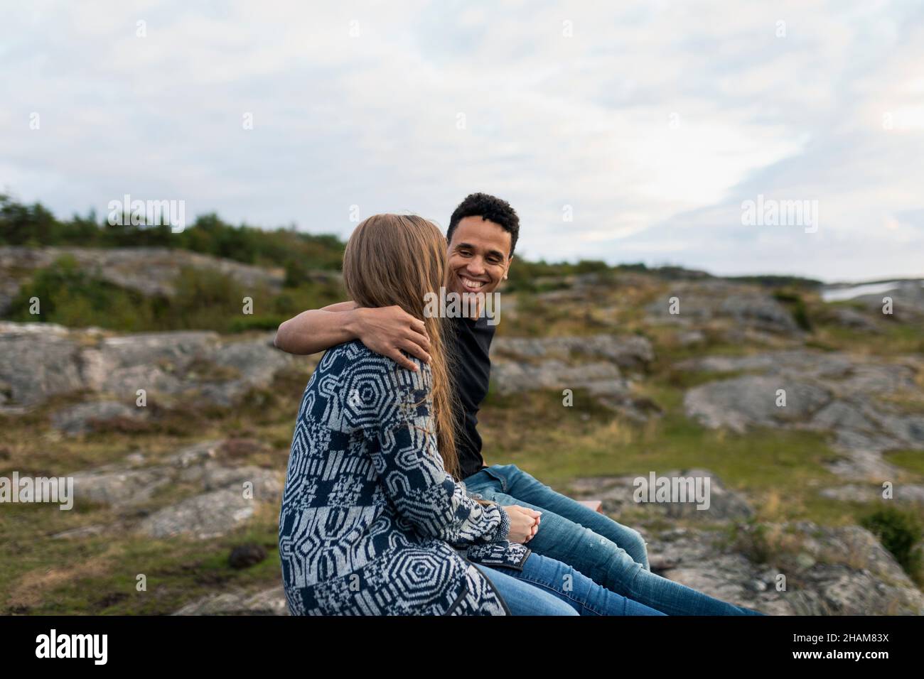 Coppia sorridente seduta su rocce e abbracciata Foto Stock