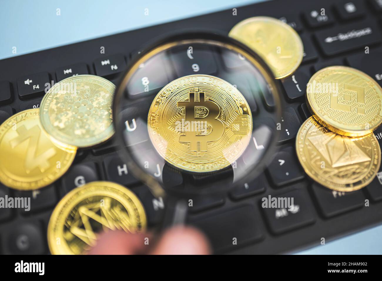 Vista ravvicinata di Bitcoin attraverso la lente di ingrandimento sulla tastiera accanto alla popolare criptovaluta Ethereum, Binance, Cardano, Zcash. Concetto di analisi del mercato Crypto. Foto Stock