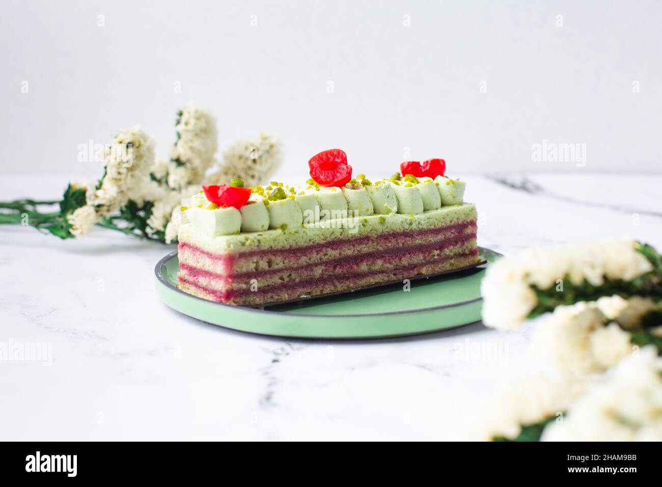 Dolce di pasticceria decorato con crema verde, ciliegia e pistacchio su sfondo marmo Foto Stock