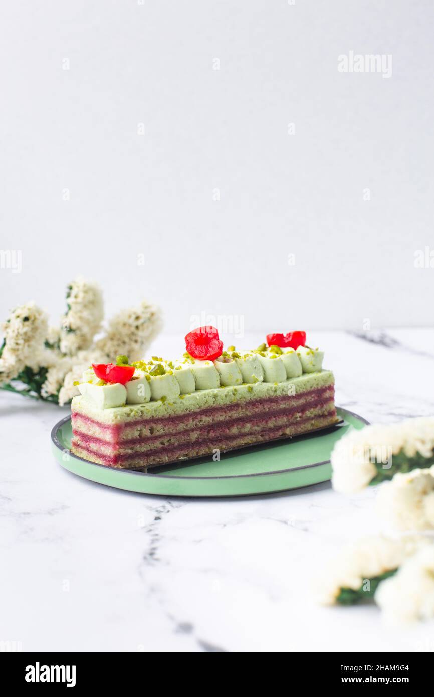 Dolce di pasticceria decorato con crema verde, ciliegia e pistacchio su sfondo marmo Foto Stock