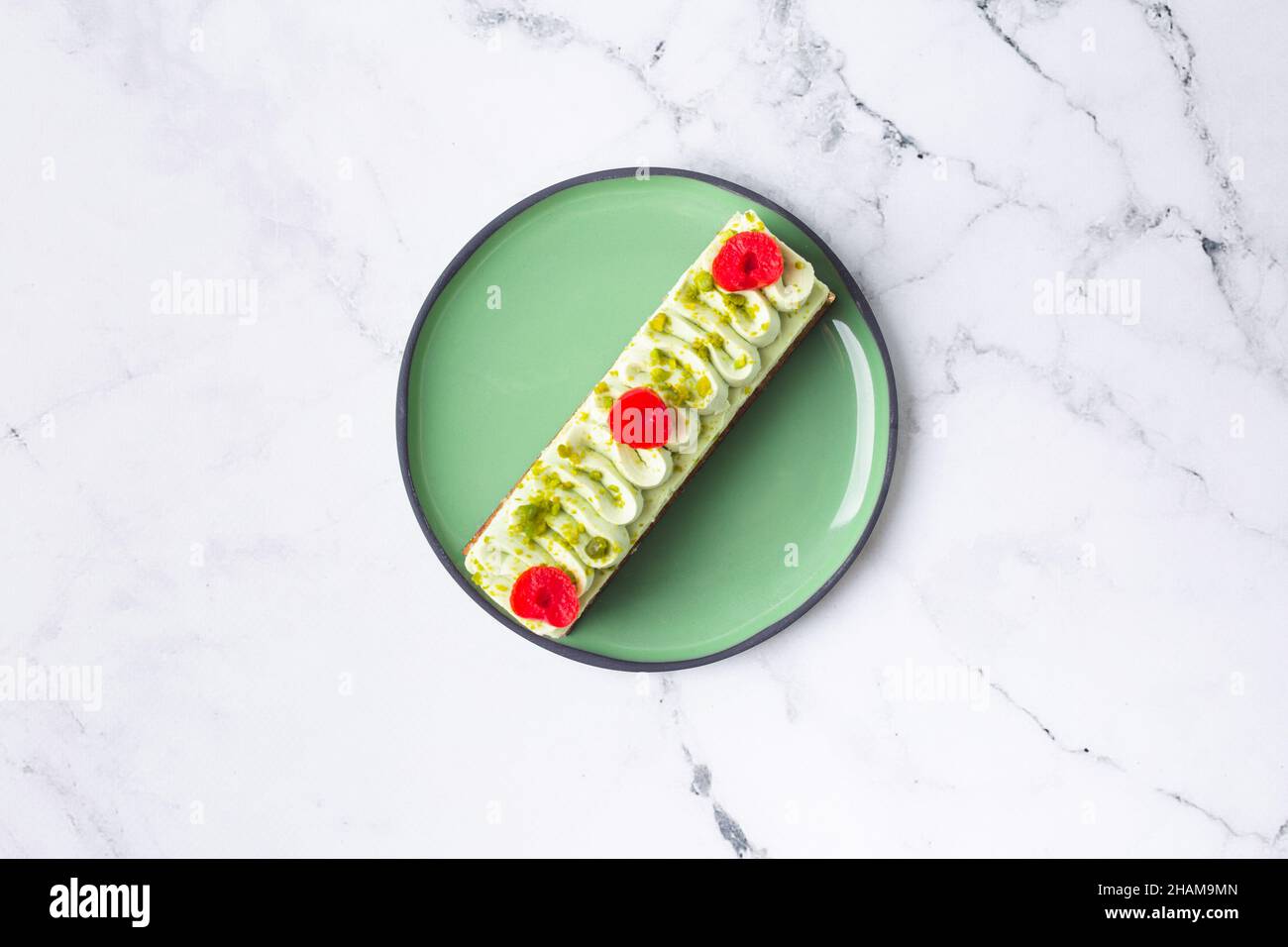 Dolce di pasticceria decorato con crema verde, ciliegia e pistacchio su sfondo marmo Foto Stock