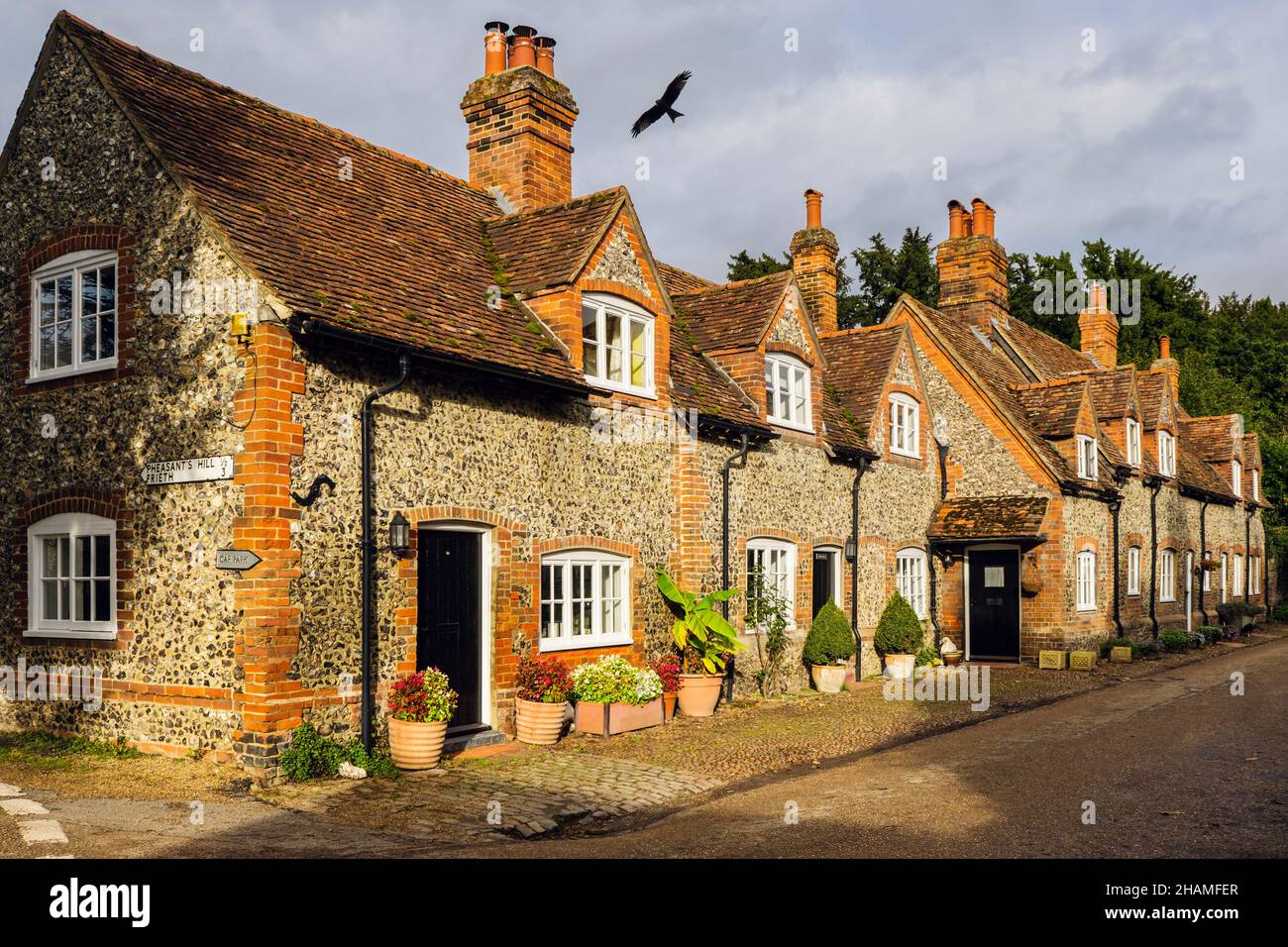 Fila di case in pietra focaia d'epoca con un aquilone rosso che vola sui tetti nel villaggio storico. Hambleden, Buckinghamshire, Inghilterra, Regno Unito, Gran Bretagna Foto Stock