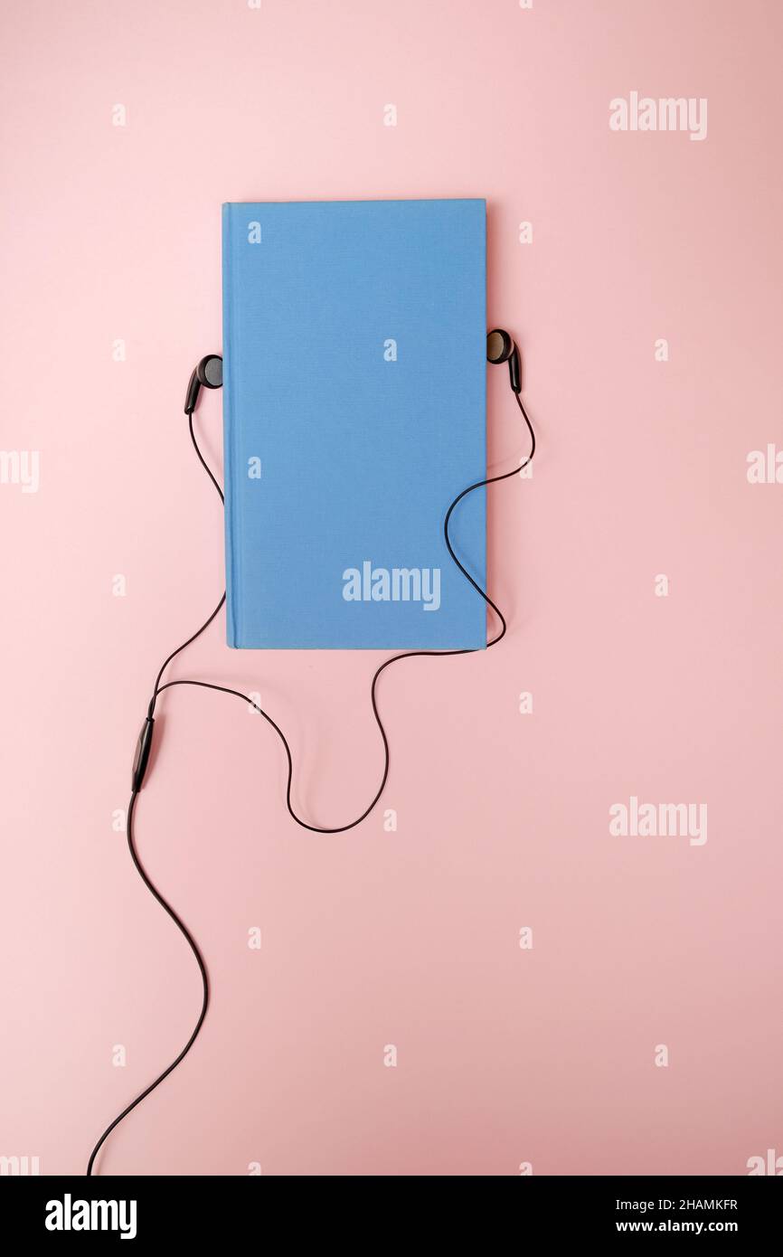 Vista dall'alto di un libro blu e delle cuffie su sfondo rosa: Il concetto di audiolibro Foto Stock