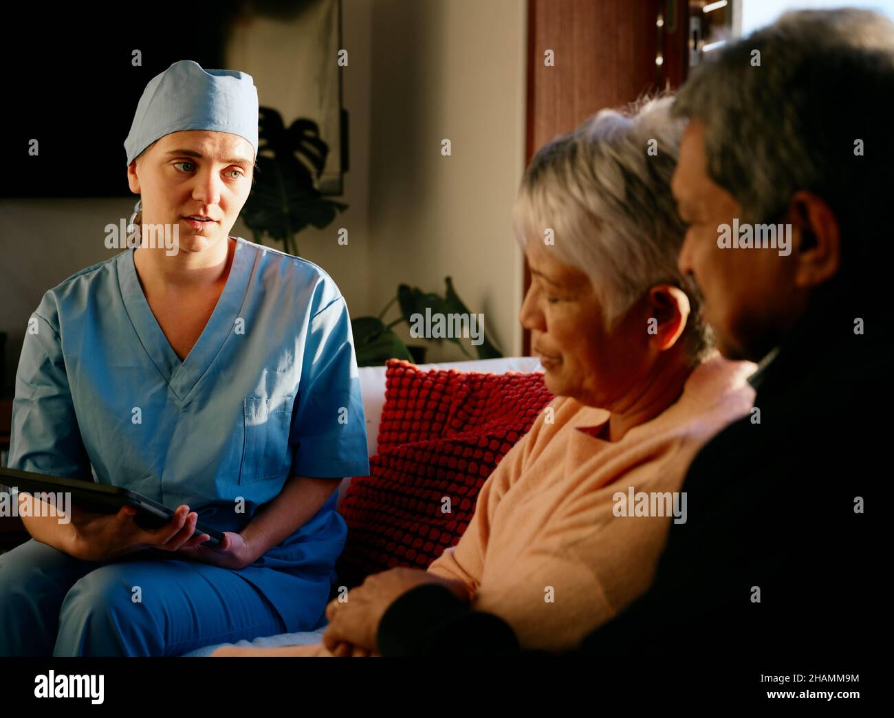 Il medico rompendo le notizie negative alla coppia multi-etnica anziana nella consultazione domestica Foto Stock