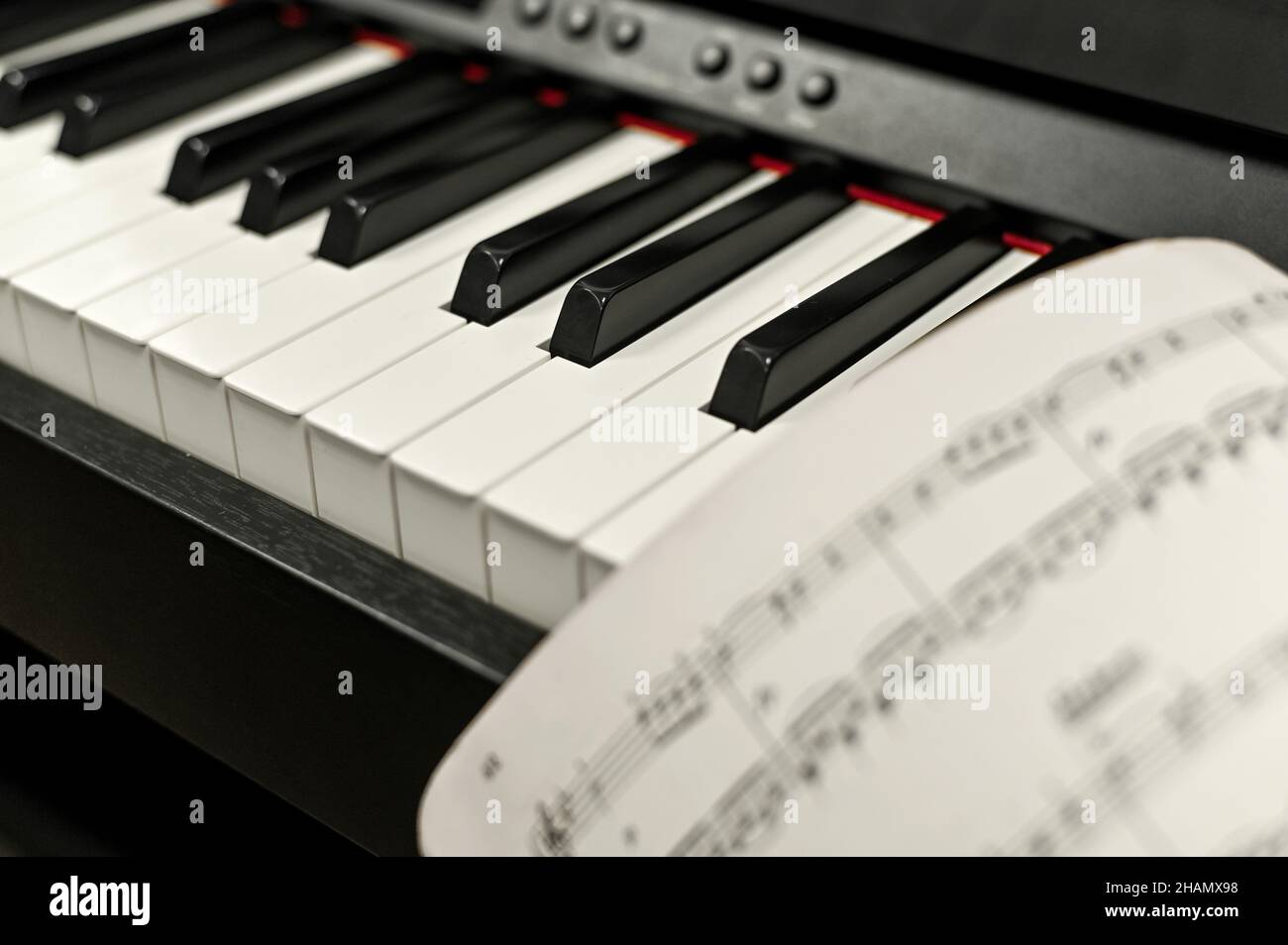primo piano dei tasti elettronici del pianoforte. foglio di carta con note musicali. Foto Stock